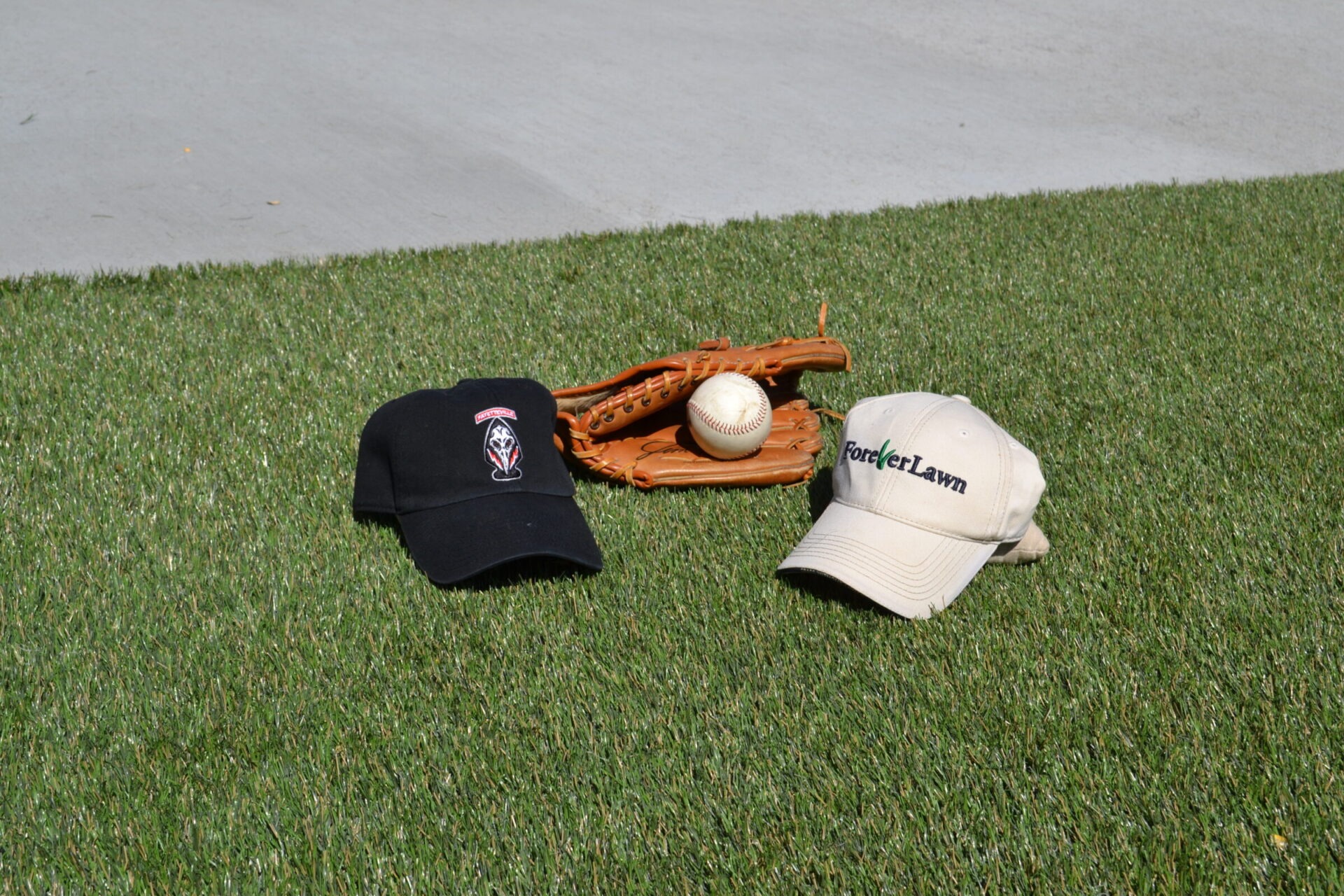Two baseball caps, a glove, and a ball are arranged on grass, suggesting recreational or sports activity, possibly related to baseball.