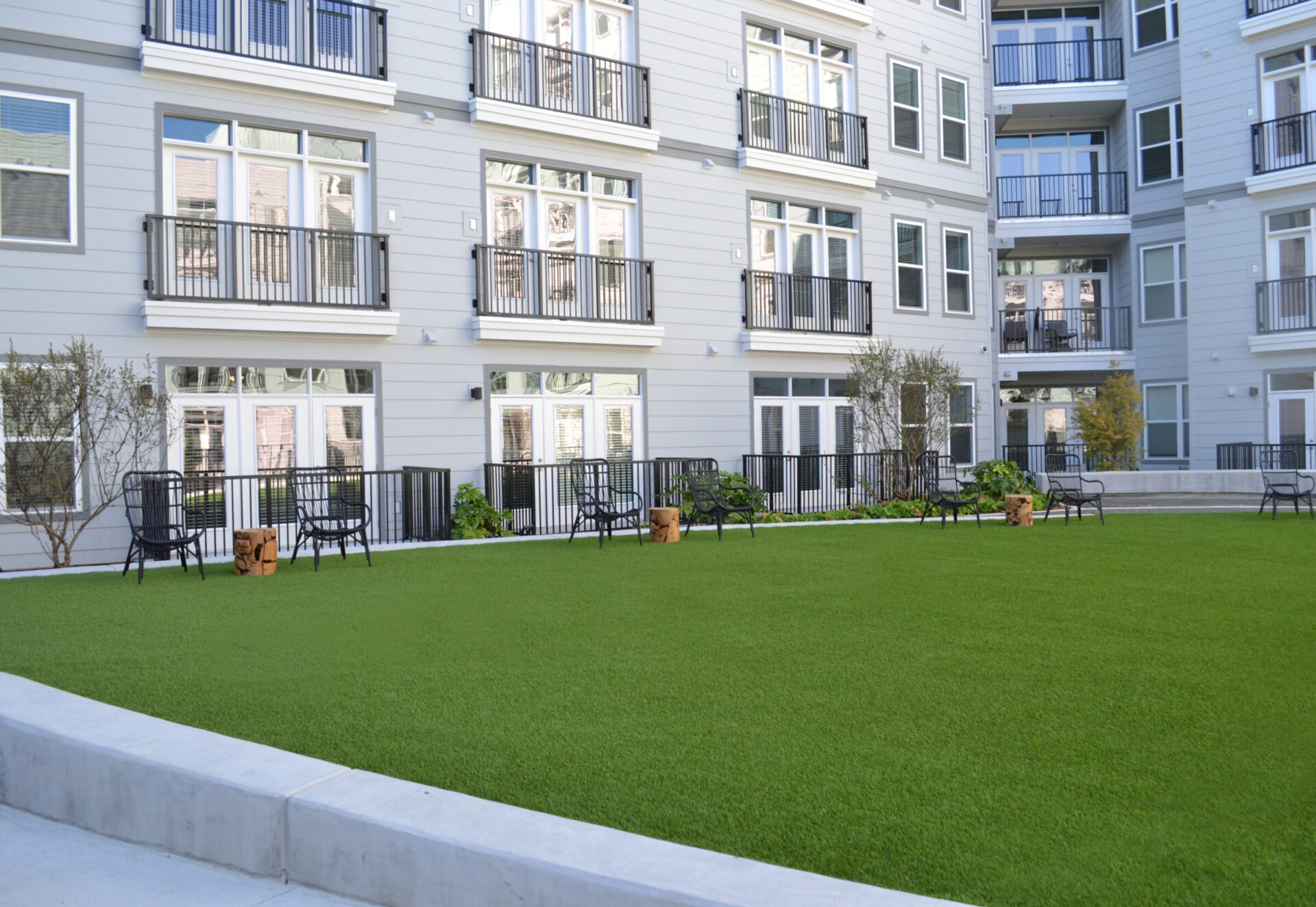 This image shows a well-manicured green space with artificial turf, surrounded by a residential building with balconies, seating areas, and decorative plants.