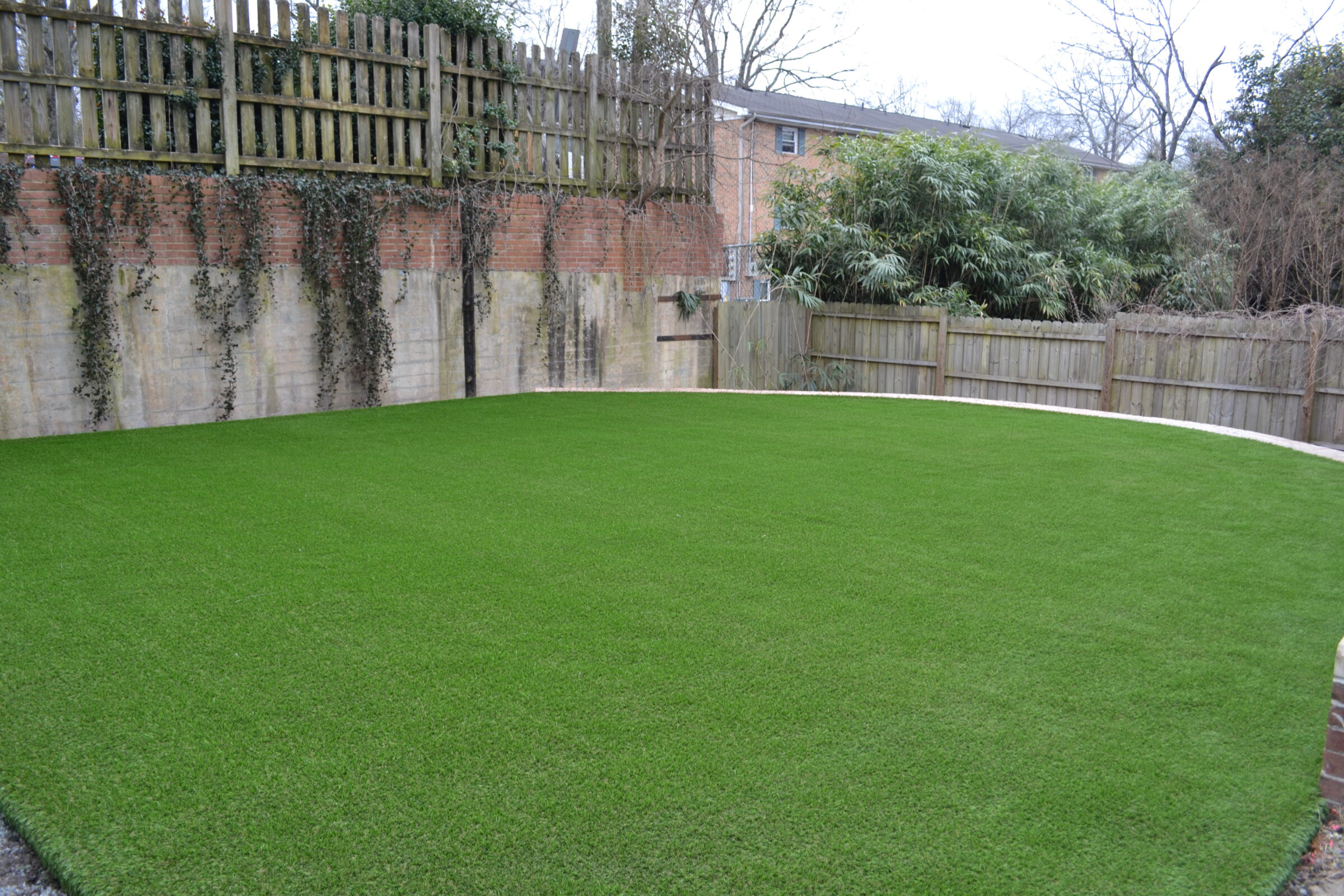 An immaculate green lawn is surrounded by a brick wall, wooden fence, and dense foliage, creating a private and serene garden space.