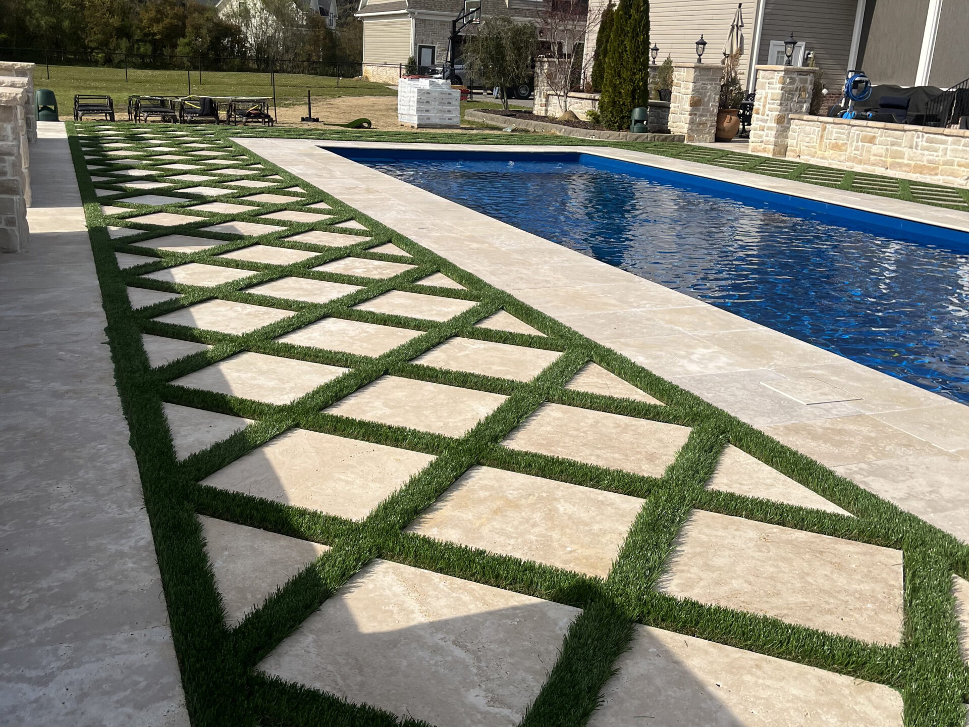 Modern poolside patio featuring a geometric stone walkway with artificial turf inlays surrounding a residential swimming pool.